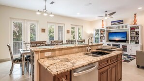 A spacious kitchen with a large island, dining area, and a TV in the living room. - It's a Jungle Out There - Tropical Pool, Sunset Views, Game Room! (Holmes Beach)
