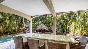 An outdoor patio with a glass-top bar, wicker chairs, a pool, and lush tropical vegetation. - It's a Jungle Out There - Tropical Pool, Sunset Views, Game Room! (Holmes Beach)