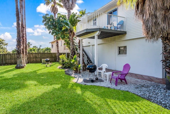 A backyard with a grill, patio chairs, and a small deck.