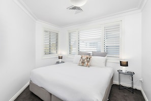 Een slaapkamer met een bed, twee nachtkastjes, een lamp en een raam met zonwering.