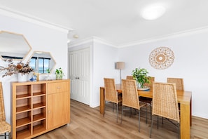 Een eethoek met een houten tafel en stoelen, een kast met planken, een spiegel en een decoratief wandobject.