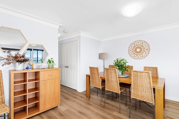 Ein Essbereich mit einem Holztisch und Stühlen, einer Schrank mit Regalen, einem Spiegel und einer Wanddekoration.