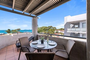 Un balcón con una mesa preparada para dos, con vistas a la costa, edificios y árboles.