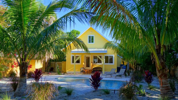 A yellow house with a swimming pool surrounded by palm trees and various plants. - Covey Cottage! Walk to Beach, Boutique Shops and City Pier (Anna Maria)