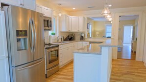 A modern kitchen with stainless steel appliances, white cabinetry, and a central island. - Covey Cottage! Walk to Beach, Boutique Shops and City Pier (Anna Maria)