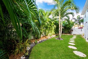 A well-maintained garden with a stone pathway, lush greenery, and a white fence.