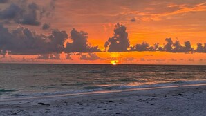 Un coucher de soleil sur une plage, avec des vagues et des nuages.