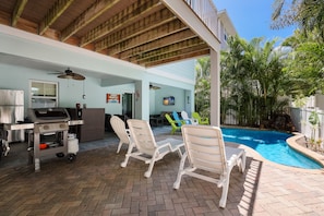 An outdoor patio with a pool, lounge chairs, a grill, and a covered seating area.
