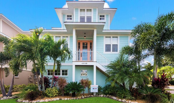 A two-story house with a balcony, a sign indicating a heated pool, and a well-maintained garden with various plants.