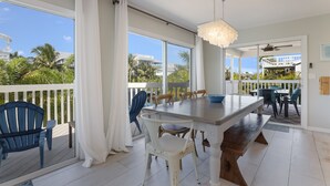 A spacious balcony with a dining area, white curtains, and a view of palm trees and buildings. - Spacious Canal front Home with Pool, Perfect For Family Vacations! (Anna Maria)