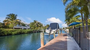 A wooden dock extending over a calm waterway, with a boat docked at the end. - Spacious Canal front Home with Pool, Perfect For Family Vacations! (Anna Maria)