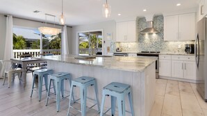 A modern kitchen with a large island, bar stools, white cabinets, and a view of the outdoors. - Spacious Canal front Home with Pool, Perfect For Family Vacations! (Anna Maria)