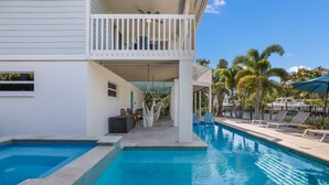 A swimming pool with a white building, a balcony, and palm trees. - Spacious Canal front Home with Pool, Perfect For Family Vacations! (Anna Maria)