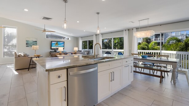A modern kitchen with a large island, white cabinetry, and a dining area with a white fence and outdoor seating. - Spacious Canal front Home with Pool, Perfect For Family Vacations! (Anna Maria)