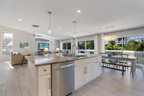 A modern kitchen with a large island, white cabinetry, and a dining area with a white fence and outdoor seating.