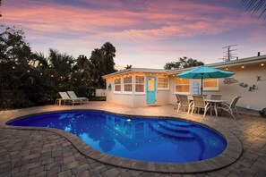 A backyard with a swimming pool, a patio with chairs, and a house with a blue door. - Close to Beach! Home with Putting Green and Pool! (Holmes Beach)