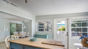 A kitchen with a wooden island, white chairs, a teal cabinet, and a window with a view of greenery.