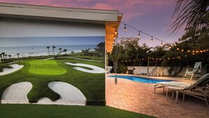 A golf course with a pool and lounge chairs, overlooking the ocean.