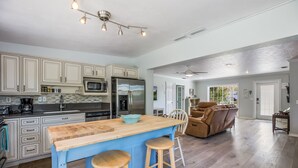 A spacious kitchen with a central island, a dining area with a brown leather sofa, and a ceiling fan.