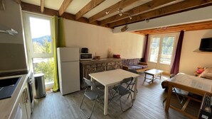 Une cuisine compacte équipée d’un réfrigérateur, d’un four à micro-ondes et de meubles de rangement en bois. On y trouve une table à manger avec des chaises, un canapé et une fenêtre avec des rideaux.