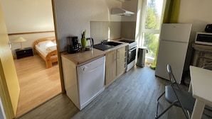Une cuisine compacte équipée d’un évier, d’une cuisinière et d’un réfrigérateur, jouxtant une chambre à coucher avec un lit et une table de chevet.