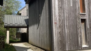 Un bâtiment en bois doté d’une porte de garage, d’une petite fenêtre et d’un chemin en béton menant à une zone abritée.