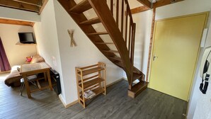 Une pièce avec un escalier en bois, une petite table avec des chaises, un téléviseur et une porte jaune.