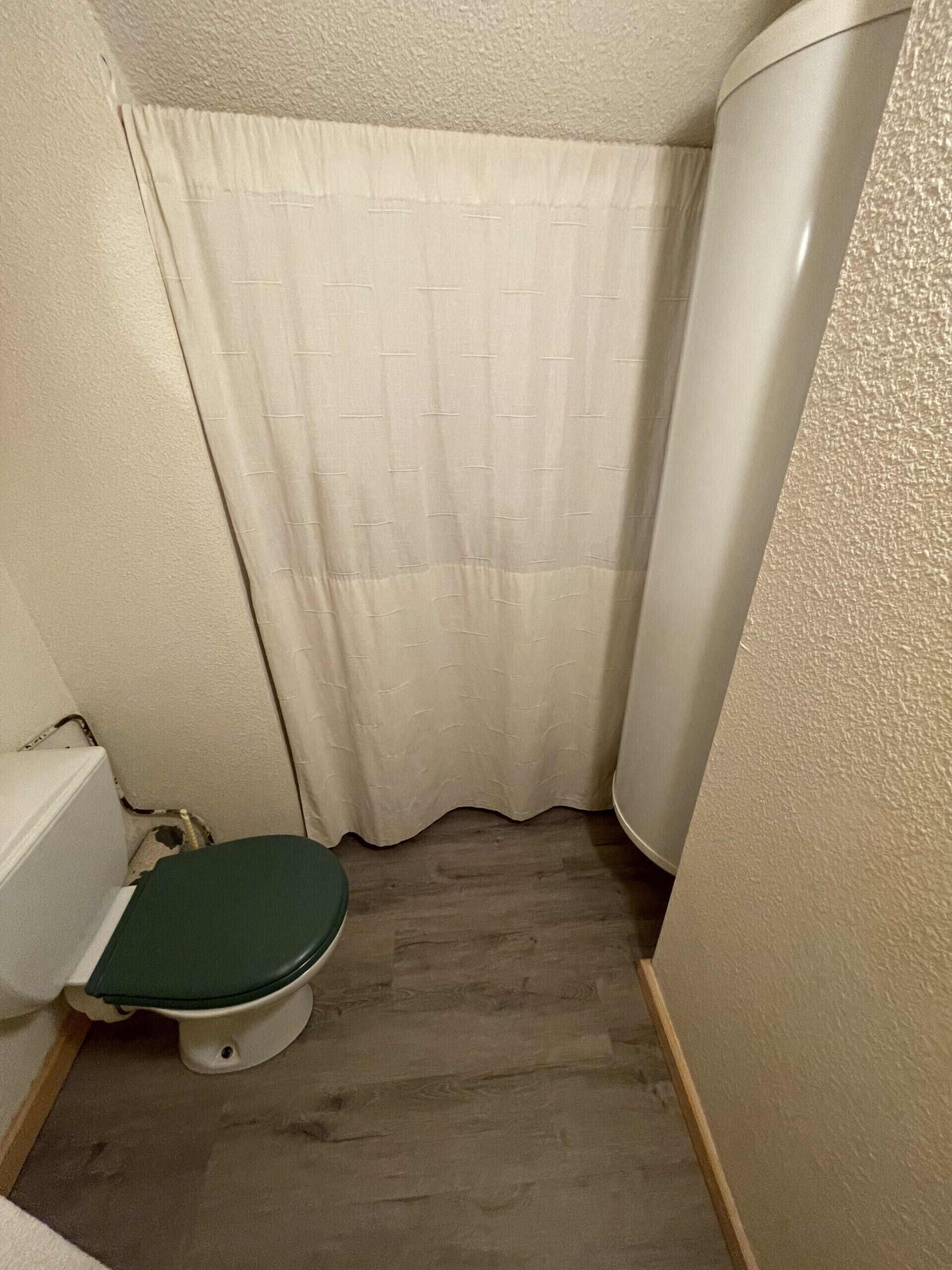 Ein kleines Badezimmer mit Toilette, grünem Sitz, weißen Wänden und einer Duschvorhang.