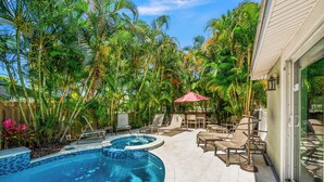 Un patio trasero con piscina, sillas de descanso y plantas tropicales.
