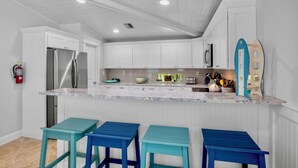 Una cocina con armarios blancos, un refrigerador de acero inoxidable, encimera de mármol y taburetes de bar azules.