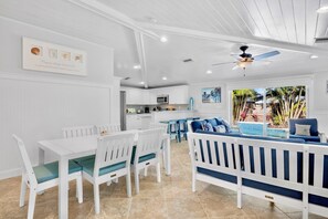 A modern kitchen with white cabinetry, a dining area with white and blue furniture, and a ceiling fan. - No Bad Days - 1.5 Blocks to Gulf Beaches, Private Heated Pool! (Holmes Beach)