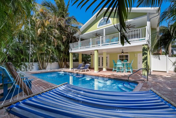 Un espace piscine aménagé avec un hamac, des chaises longues et un balcon donnant sur la piscine.