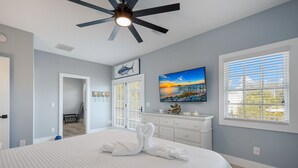 Une chambre à coucher avec un lit, un ventilateur de plafond, un tableau, une commode et une fenêtre avec des stores.