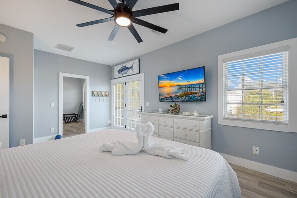 A bedroom with a bed, a ceiling fan, a painting, a dresser, and a window with blinds.
