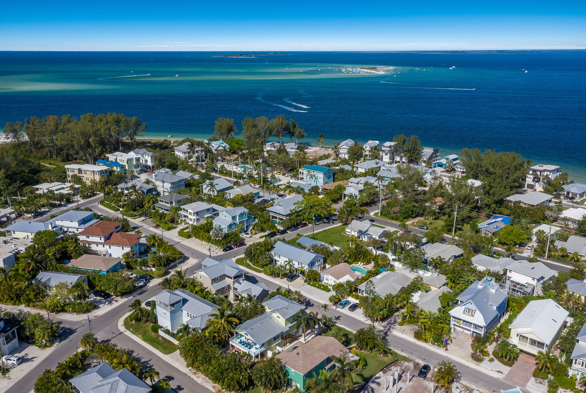 An aerial view of a coastal residential area with houses, roads, and a clear view of the ocean.