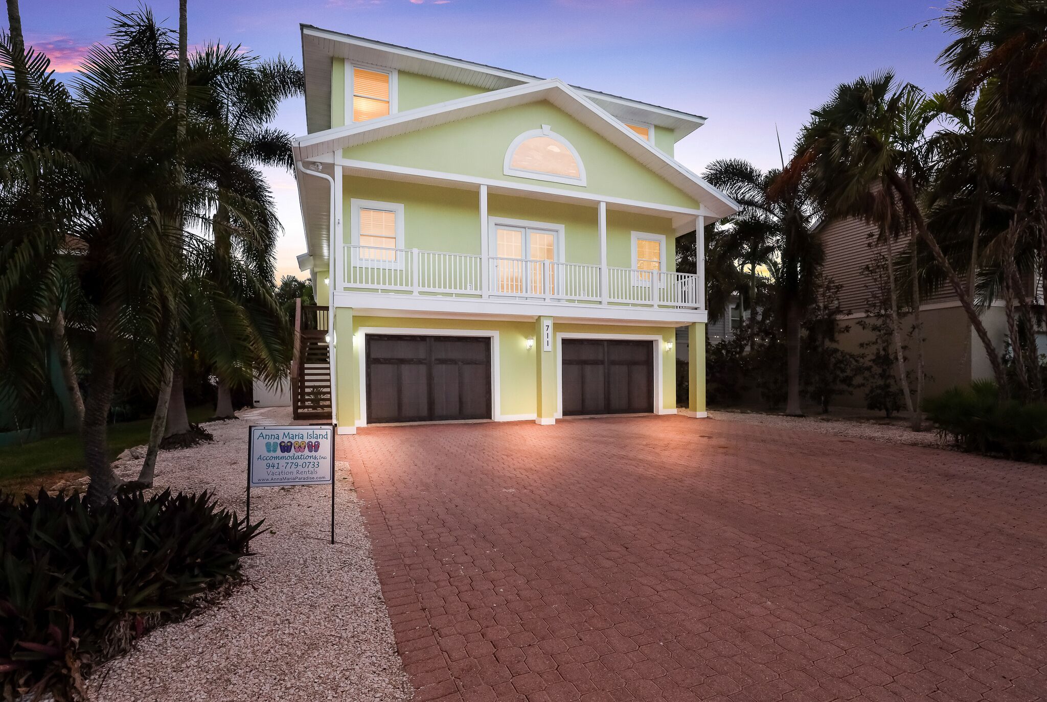 Une maison à deux étages avec un balcon, deux garages et une enseigne indiquant « Anna Maria Island Accommodations ».