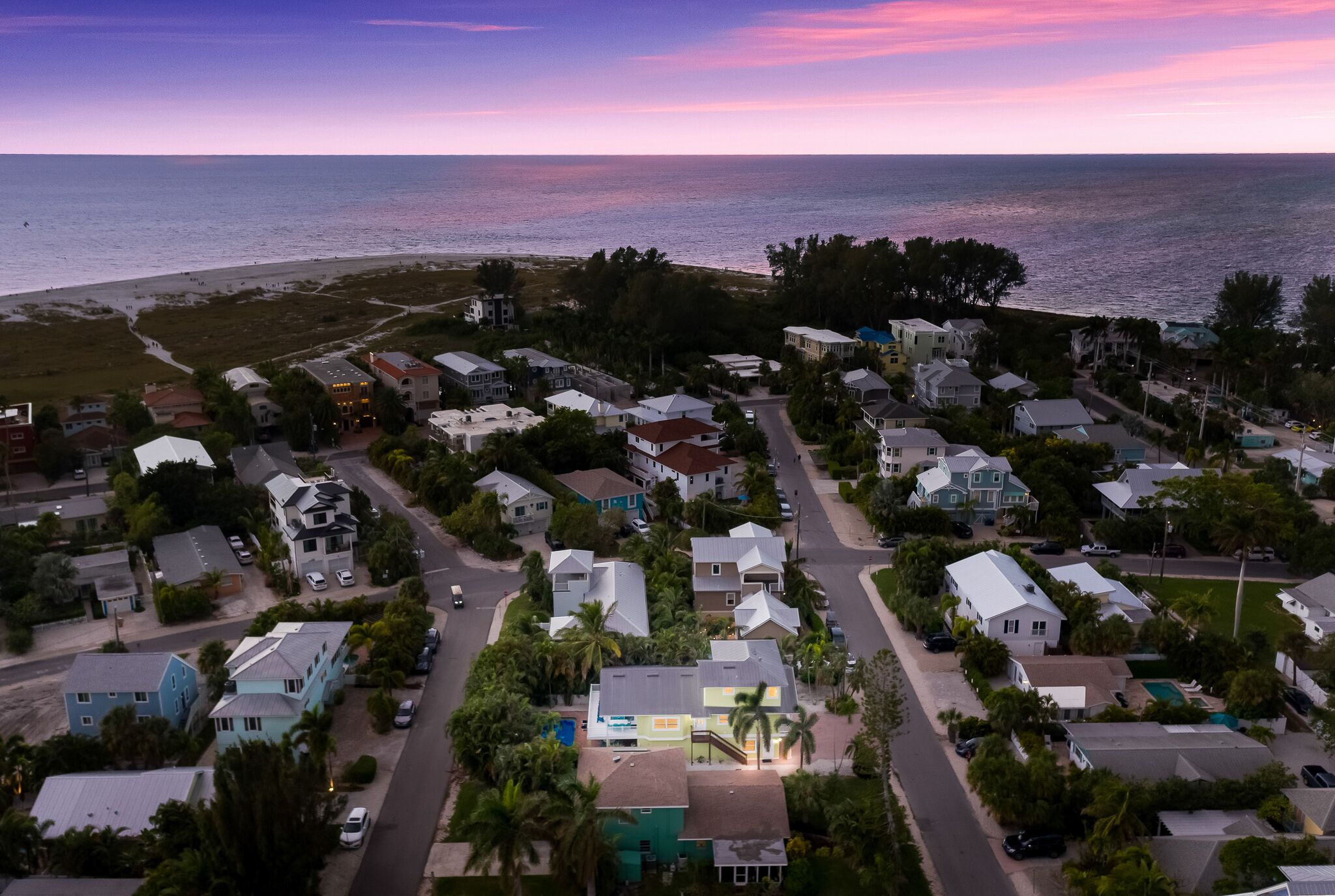 An aerial view of a residential area with houses, streets, and a beach in the background.
