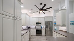 Une cuisine moderne avec des meubles blancs, des appareils en acier inoxydable et un ventilateur de plafond.