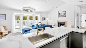 Uma cozinha moderna com bancada de mármore branco, pia embutida e um sofá azul na área de estar adjacente.