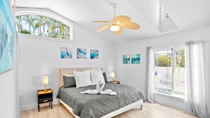 Quarto moderno com cama, ventilador de teto, obras de arte nas paredes e janela com cortinas.