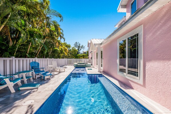 A swimming pool with lounge chairs and a white fence, surrounded by palm trees.