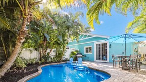 A swimming pool with a brick patio, surrounded by palm trees and a house with a blue exterior. - Beautiful Villa near the Beach with Pool! - Mermaid's Hideaway (Holmes Beach)