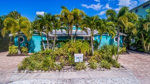 A hotel with a turquoise facade, a heated pool, and lush tropical landscaping. - Beautiful Villa near the Beach with Pool! - Mermaid's Hideaway (Holmes Beach)