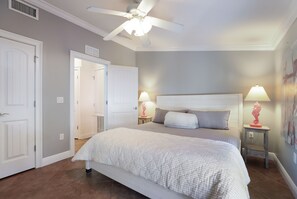 Une chambre à coucher avec un lit, deux tables de chevet avec des lampes, un ventilateur de plafond et une porte.
