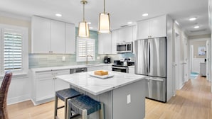 A modern kitchen with white cabinets, stainless steel appliances, and a central island with bar stools. - Beautiful Home with Pool and Outside Living Area! Near the Beach (Anna Maria)