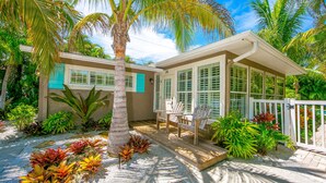 A house with a covered porch, surrounded by tropical plants and palm trees. - Beautiful Home with Pool and Outside Living Area! Near the Beach (Anna Maria)