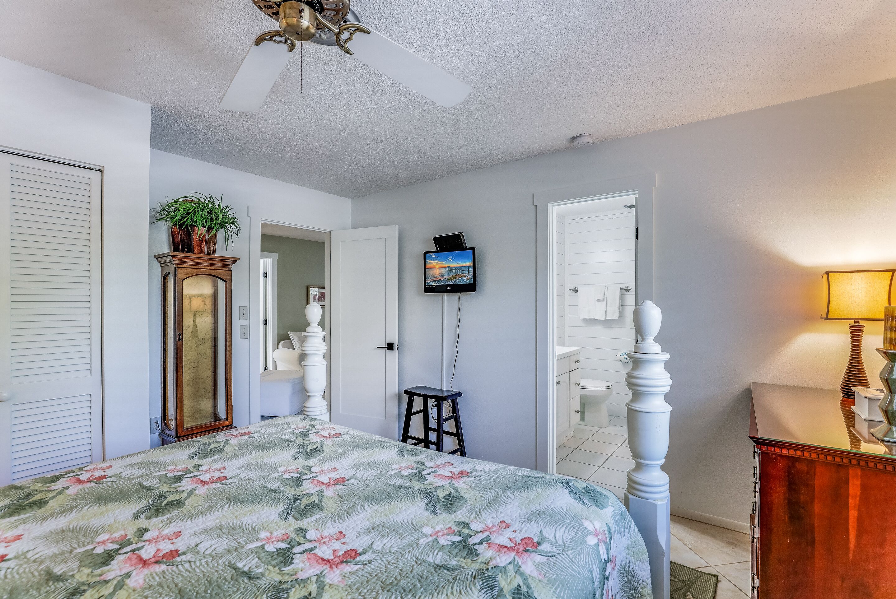A bedroom with a bed, a ceiling fan, a television, a mirror, and a dresser.