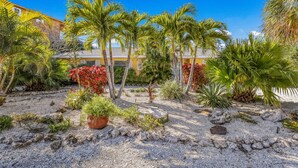 A courtyard with palm trees, a large potted plant, and a building with a yellow facade. - Quiet North End Home Only 2 Blocks to Beach with Private Pool (Anna Maria)