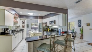 A modern kitchen with white cabinets, a central island with bar stools, and a microwave above the island. - Quiet North End Home Only 2 Blocks to Beach with Private Pool (Anna Maria)
