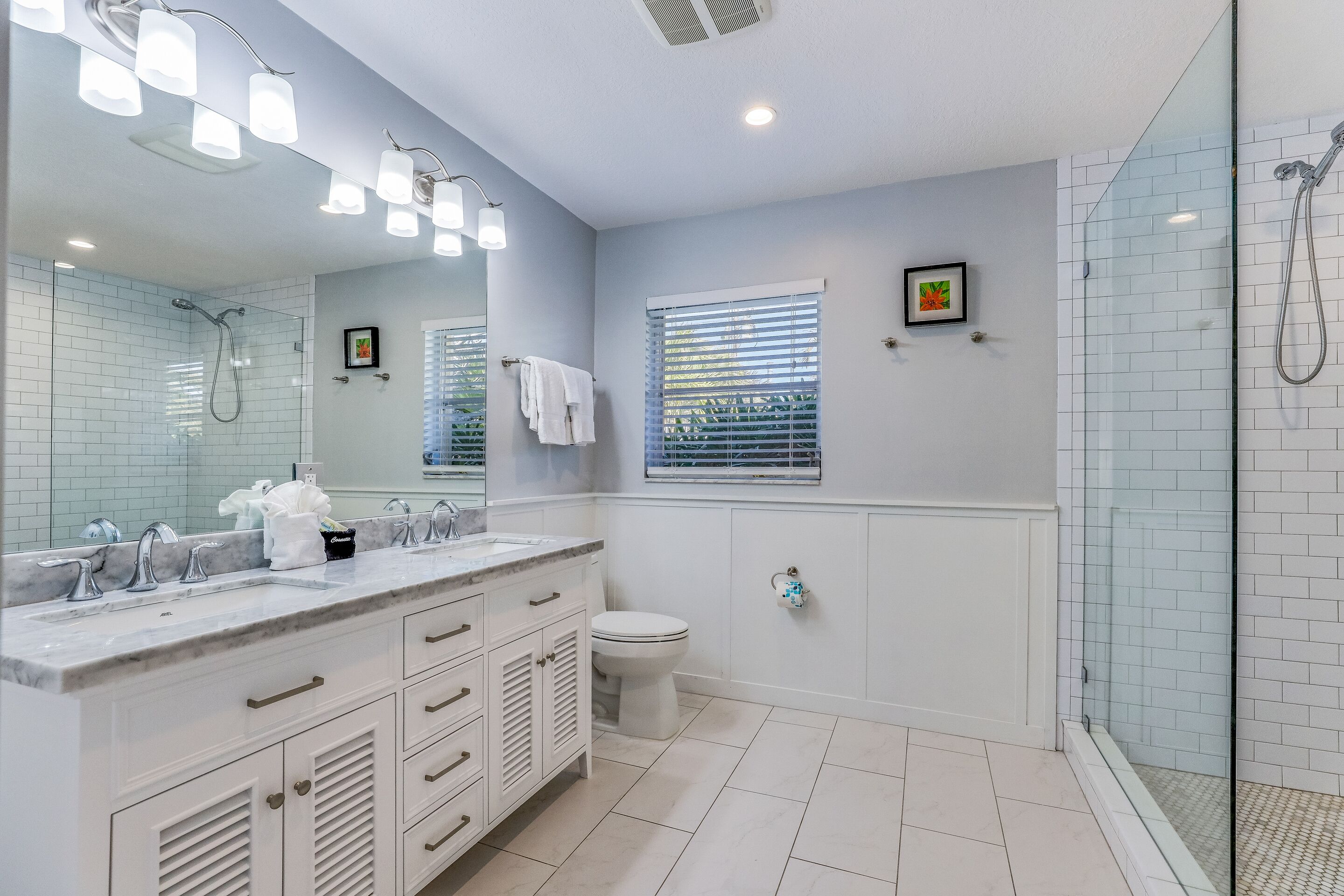 A bathroom with a large mirror, a shower, a toilet, and a vanity with a sink.